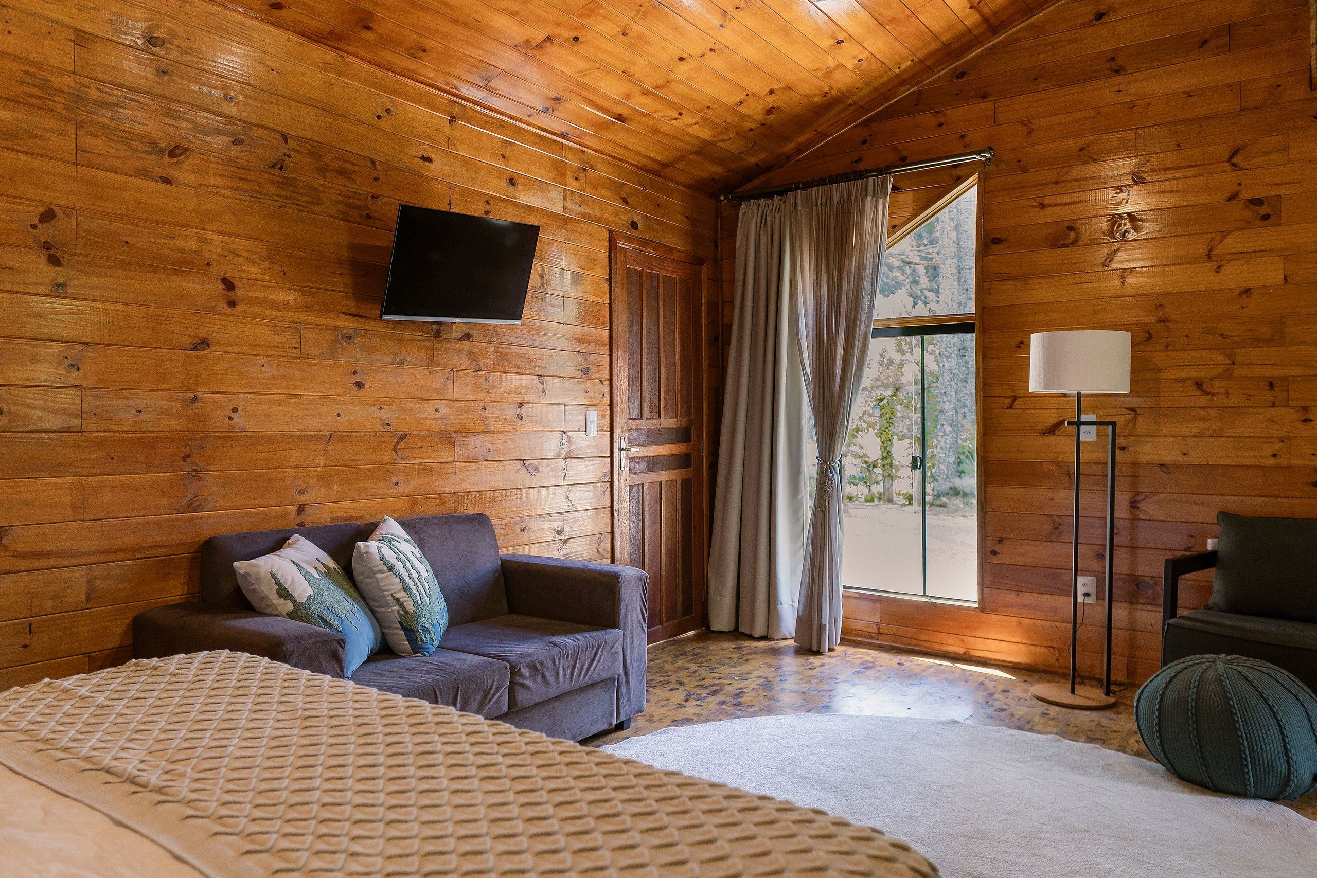 Una habitación con paneles de madera, un sofá, una cama, una lámpara de pie y un televisor montado en la pared.