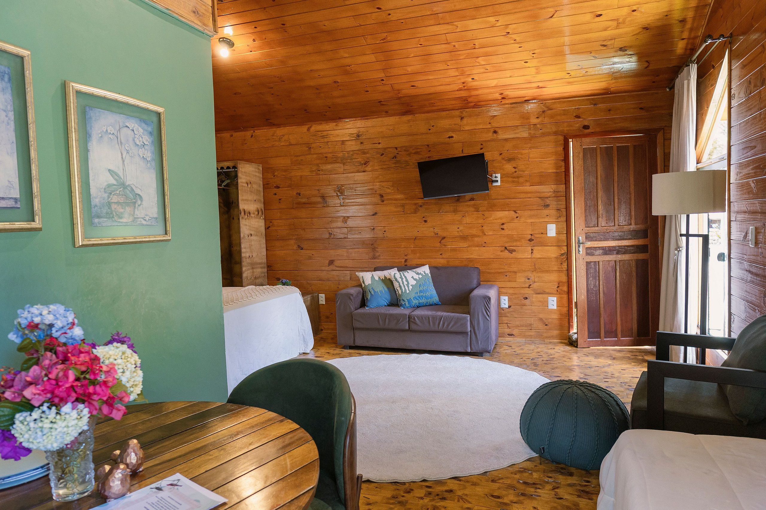 Ein Interieur einer Holzhütte mit einer Couch, einem Fernseher, einem Esstisch mit Stühlen und einer Blumenvase.