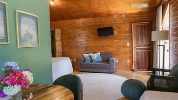 Ein Interieur einer Holzhütte mit einer Couch, einem Fernseher, einem Esstisch mit Stühlen und einer Blumenvase.