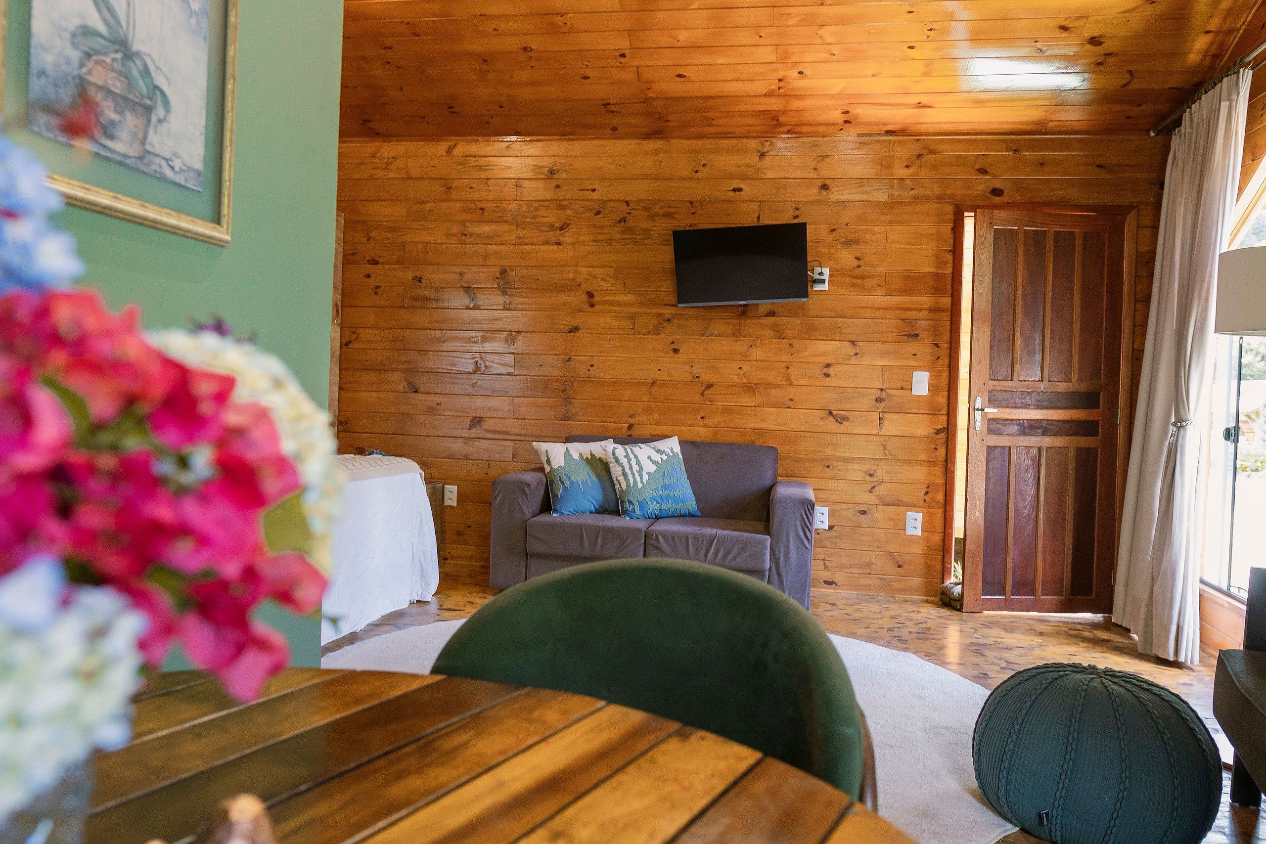 Quarto com painéis de madeira, um sofá, uma televisão e uma porta que dá para o exterior.
