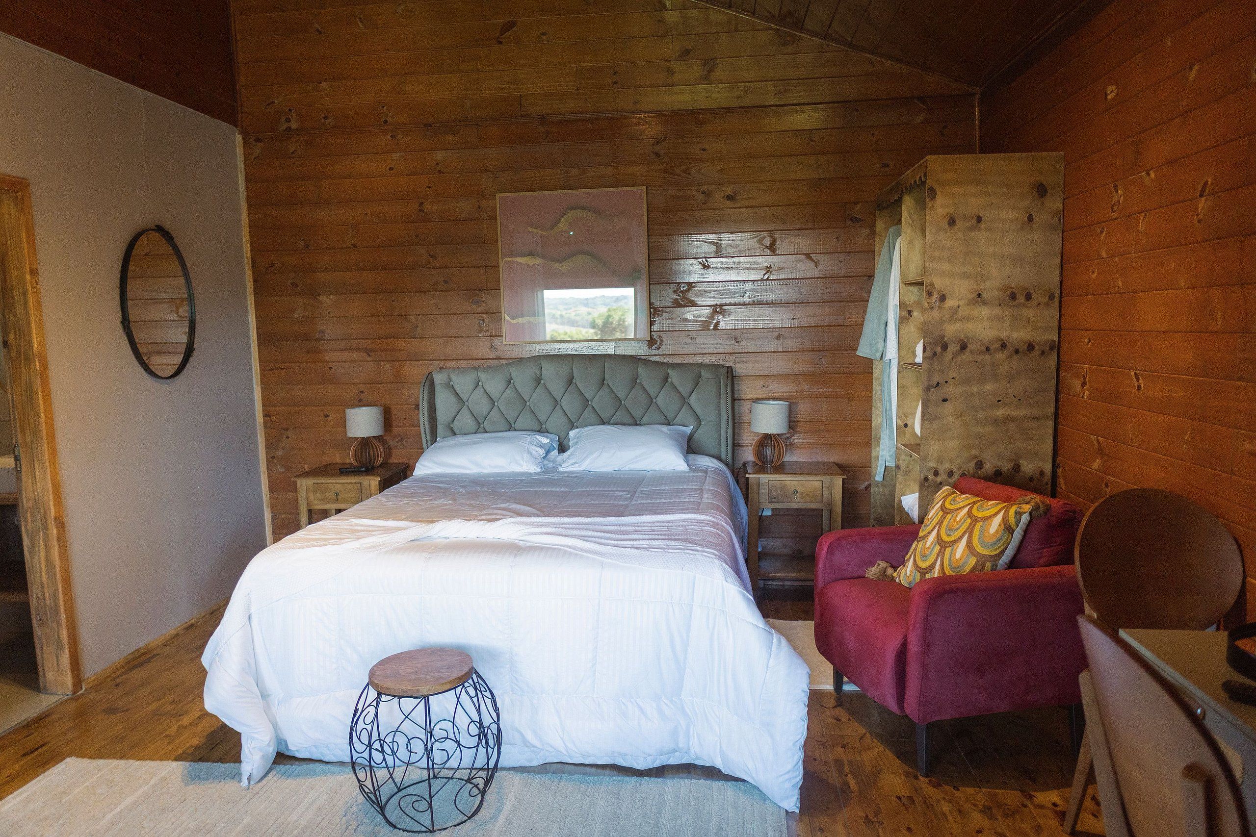 Un dormitorio con paneles de madera, una cama grande, una silla roja y una mesita.