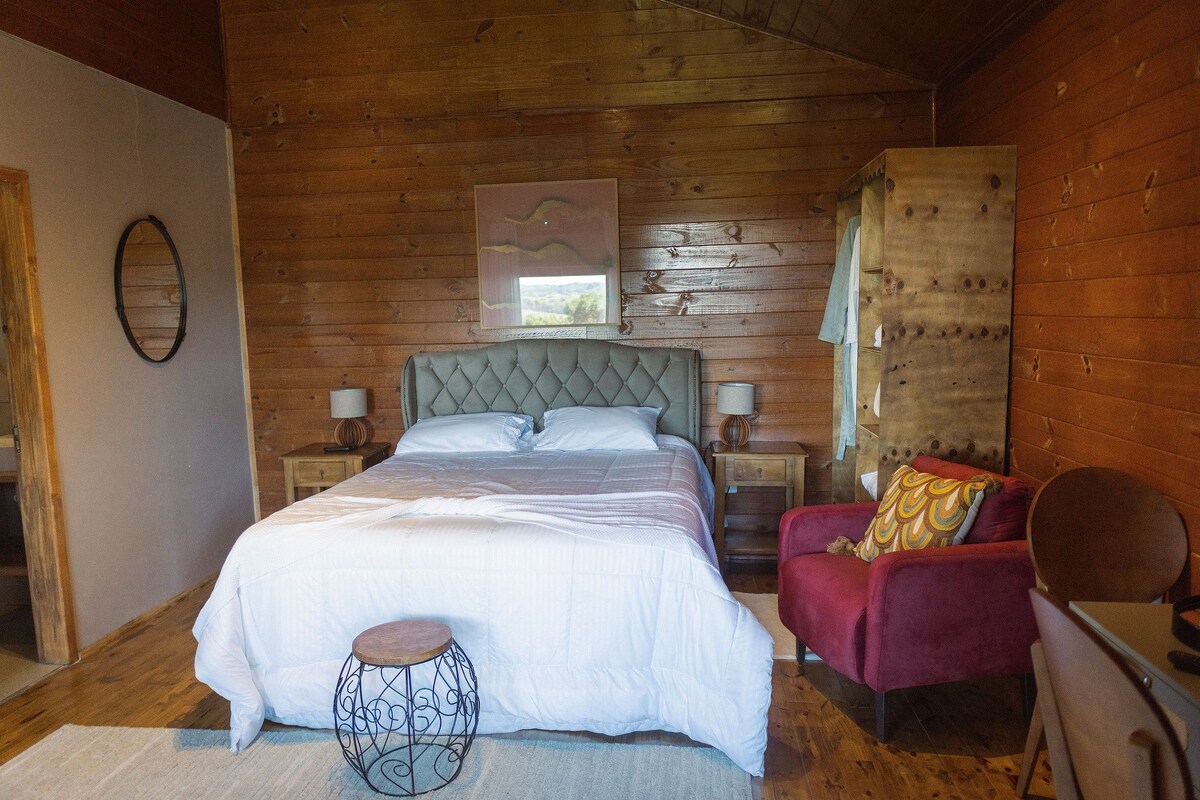 Un dormitorio con paneles de madera, una cama grande, una silla roja y una mesita.