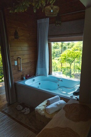 Habitación con una bañera grande, una pared de madera, una ventana con vista a árboles y un colgador de luz.