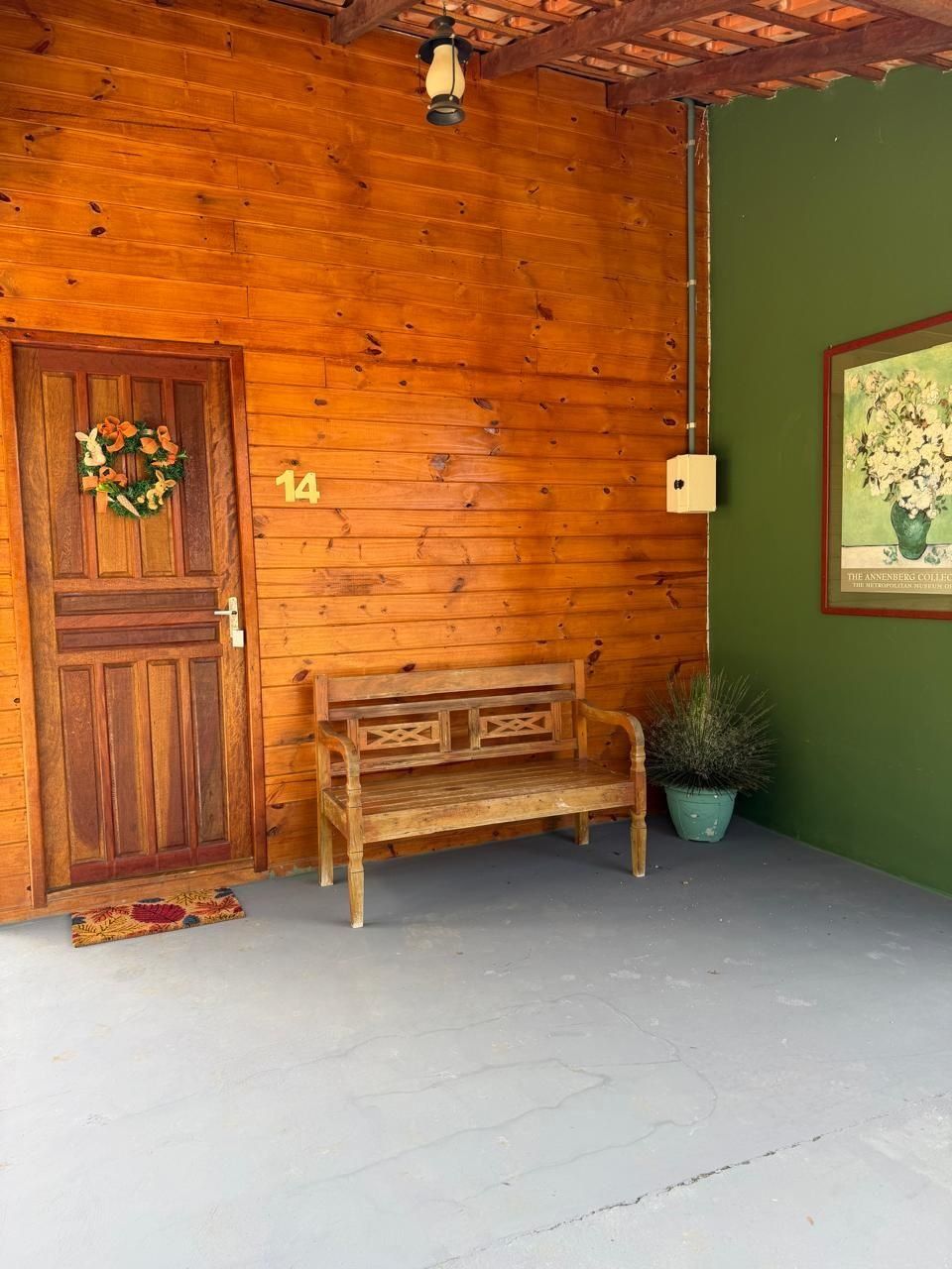 A wooden exterior with a door, number 14, a bench, a potted plant, and a wall-mounted light fixture.