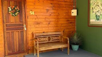 A wooden exterior with a door, number 14, a bench, a potted plant, and a wall-mounted light fixture.