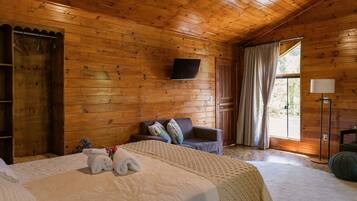 A wooden cabin room with a bed, a sofa, a TV, and a window with curtains.