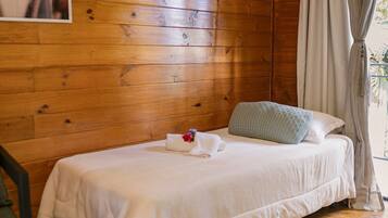 Una habitación tipo cabaña de madera con una cama individual, una silla y una ventana con cortinas.