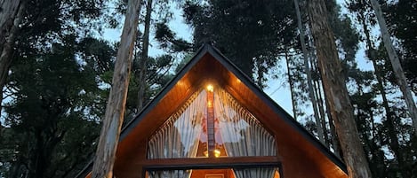A cabin with a stone foundation, wooden exterior, and a large window with curtains.