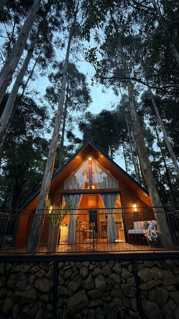 Una cabaña con base de piedra, fachada de madera y un ventanal con cortinas.