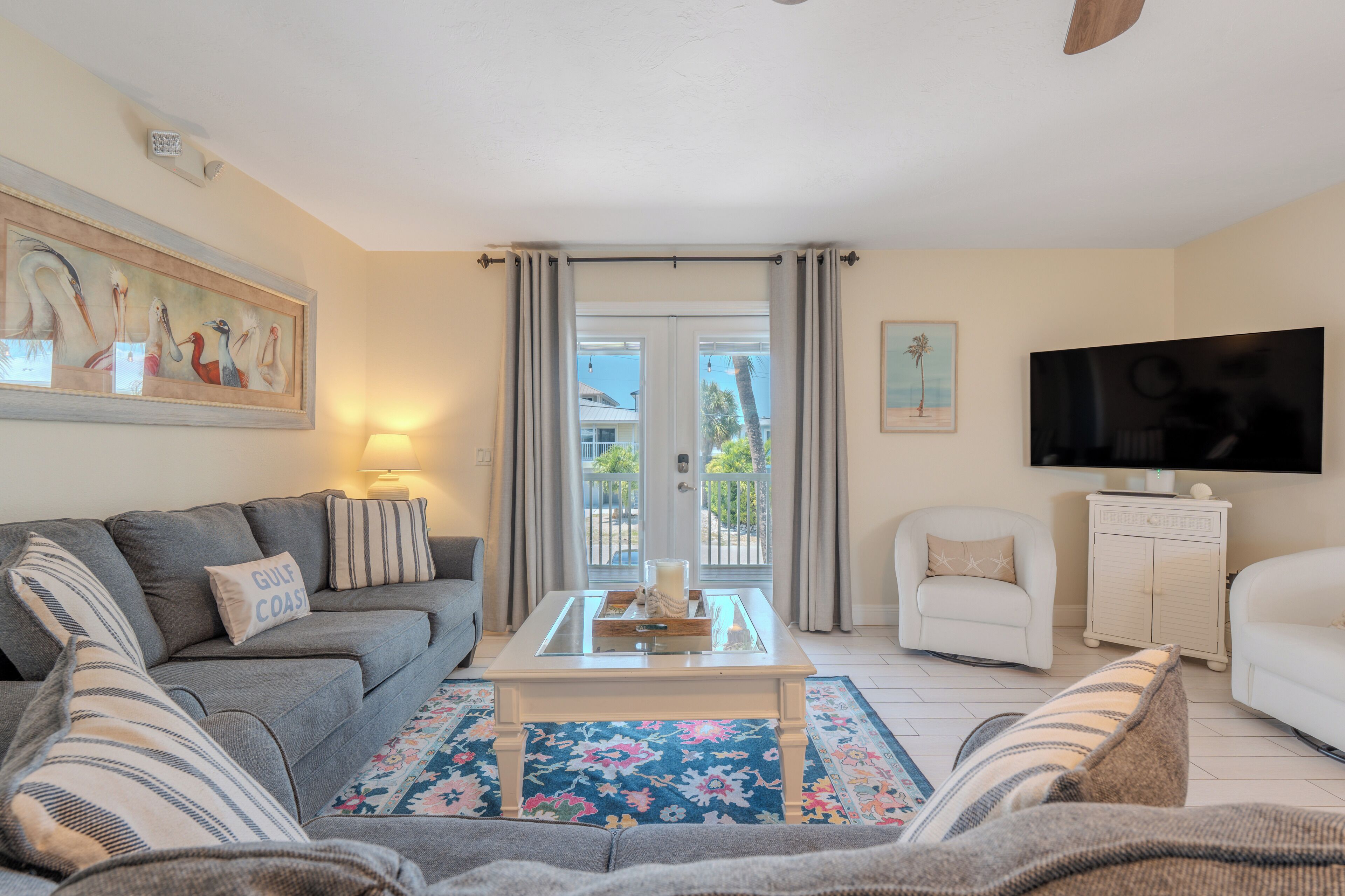 Un salon comprenant un canapé, des fauteuils, une table basse, un téléviseur et un balcon avec des rideaux.