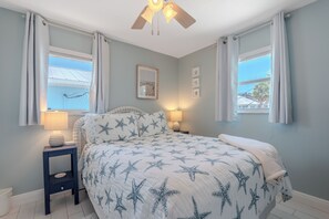 Ein Schlafzimmer mit einem Bett, zwei Nachttischlampen, einem Deckenventilator und einem Fenster mit Vorhängen.