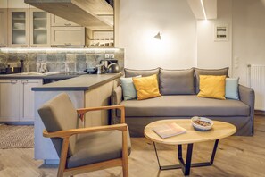 A modern kitchen with a built-in island, a grey sofa with yellow cushions, a wooden chair, and a round coffee table.