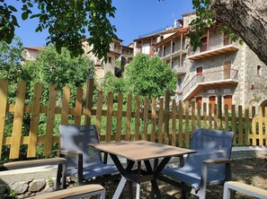 Une clôture en bois, une table et des chaises dans un espace jardin, avec des bâtiments en pierre en arrière-plan.
