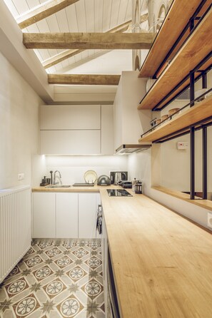 A kitchen with wooden beams, white cabinets, a patterned tile floor, and a wooden countertop.