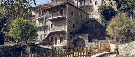 A stone building with a balcony, a wooden fence, and a stone wall.