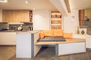 A modern kitchen with wooden cabinets, a built-in seating area with cushions, and a dining table.