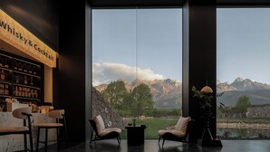 A bar area with a whiskey and cocktail sign, two chairs, a table, and a view of mountains through large windows. - Tangting Hidden Hotel (Lijiang)