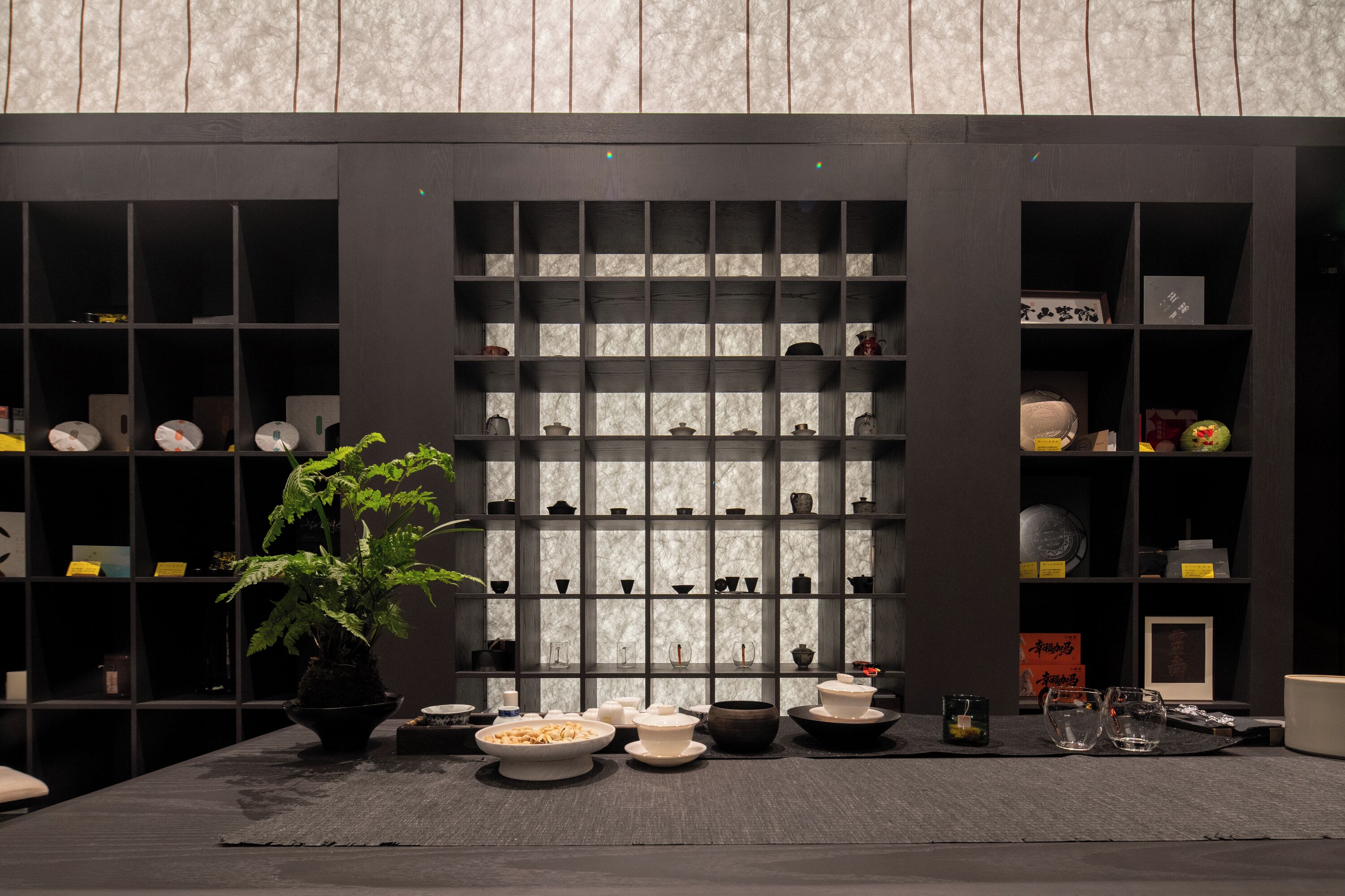 Une pièce avec une bibliothèque en bois sombre, une plante en pot et divers bols et assiettes disposés sur une table.