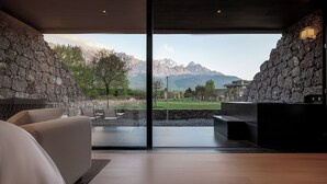 A modern room with a large window, stone walls, a sofa, and a view of mountains. - Tangting Hidden Hotel (Lijiang)