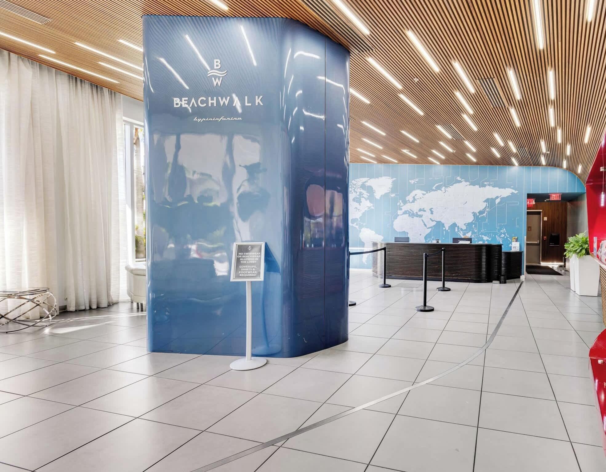 Un hall d’entrée moderne avec un comptoir d’accueil, un kiosque d’information bleu et une carte du monde affichée au mur.