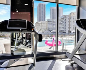 A gym with treadmills and exercise equipment, large windows with a view of high-rise buildings and a pool area. - Stylish 1BR, Bay View Balcony, Resort & Beach (Hallandale Beach)