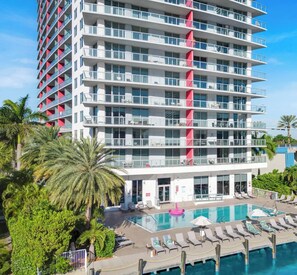 A multi-story hotel with a pool area, including lounge chairs and a poolside bar. - Stylish 1BR, Bay View Balcony, Resort & Beach (Hallandale Beach)
