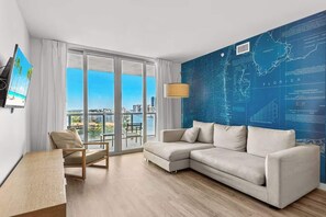 A modern living room with a large window, a sofa, a chair, and a map wall. - Stylish 1BR, Bay View Balcony, Resort & Beach (Hallandale Beach)