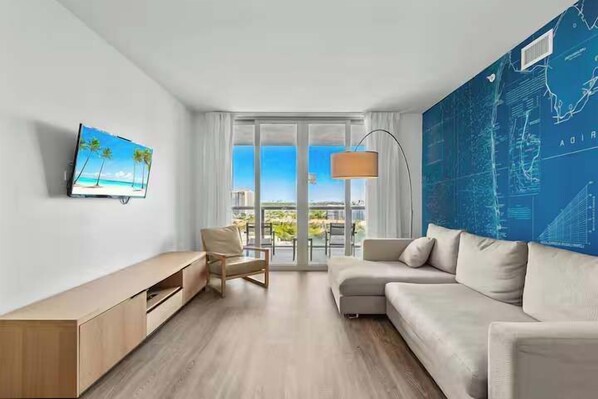 Ein modernes Hotelzimmer mit großem Fenster, Flachbildfernseher, einer Couch, einem Sessel und einer Karte an der Wand.