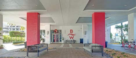 Un hall d’entrée spacieux au design moderne, avec un logo bien visible sur le mur, des espaces de détente et une vue sur la façade de l’immeuble.