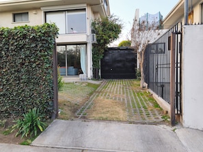 A residential area with a paved driveway, a black gate, and a hedge.