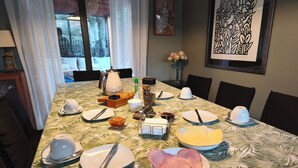 A dining table set with plates, cutlery, and condiments, with a view of the outdoors through large windows.