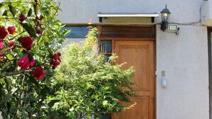 A residential building with a wooden front door, a small window above the door, and a potted plant to the right.