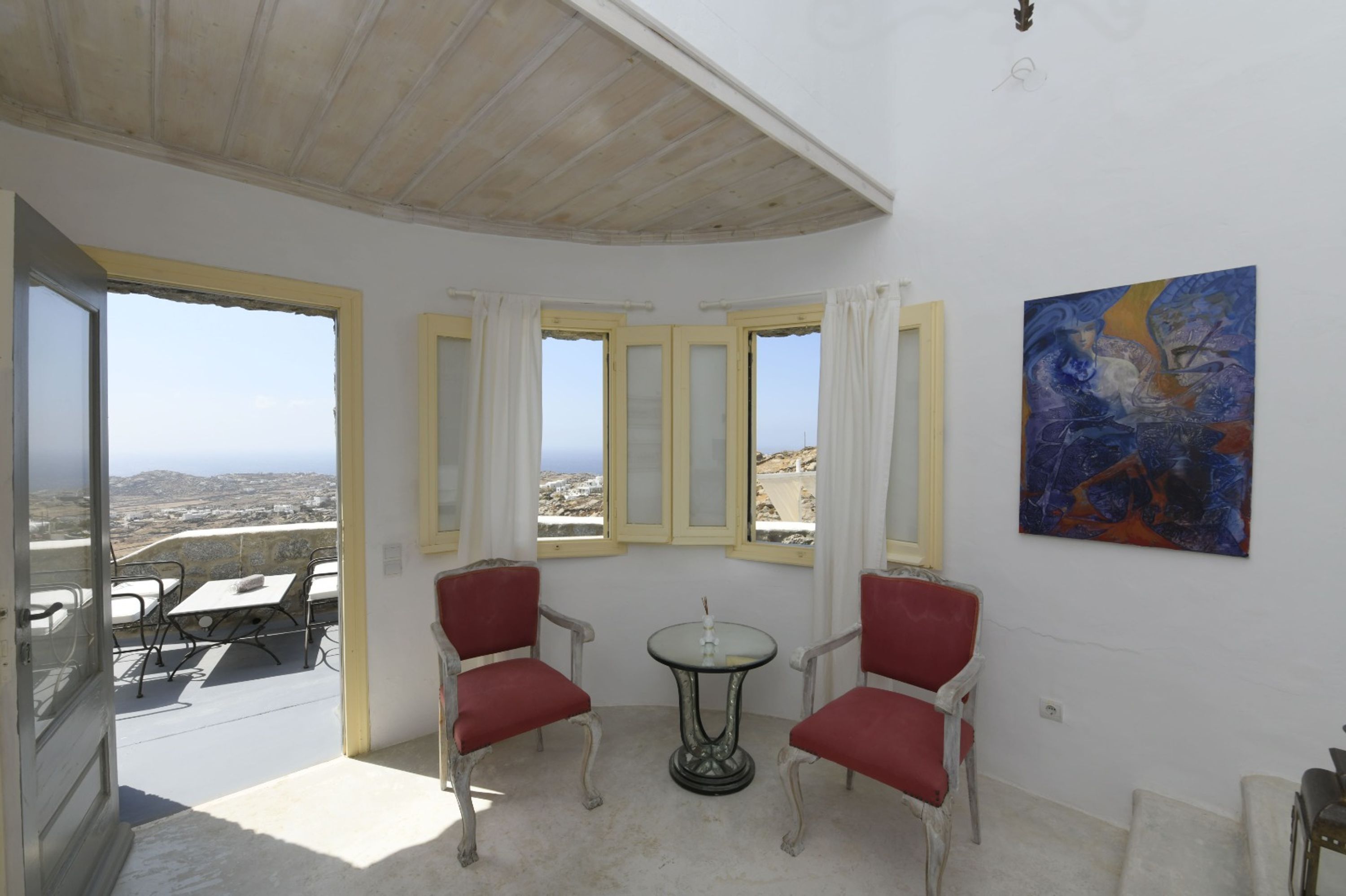 A room with a balcony, a table with chairs, and a painting on the wall.