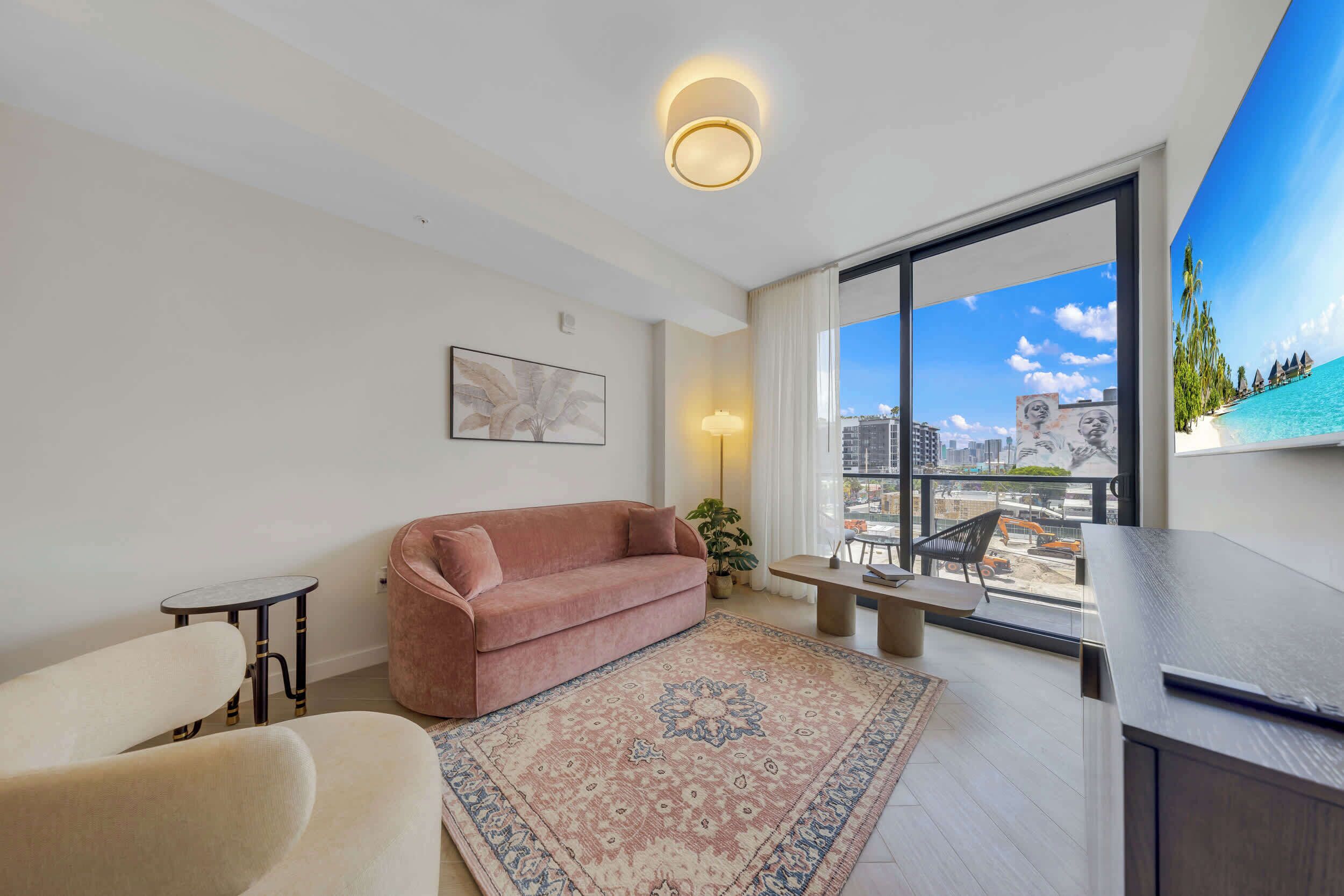 A modern living room with a sofa, a small table, a chair, a large window with a view of the city, and a painting on the wall.
