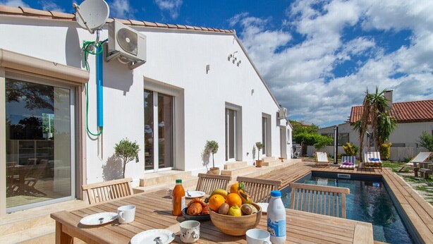 A modern house with a swimming pool, outdoor seating, and a dining area with breakfast items.