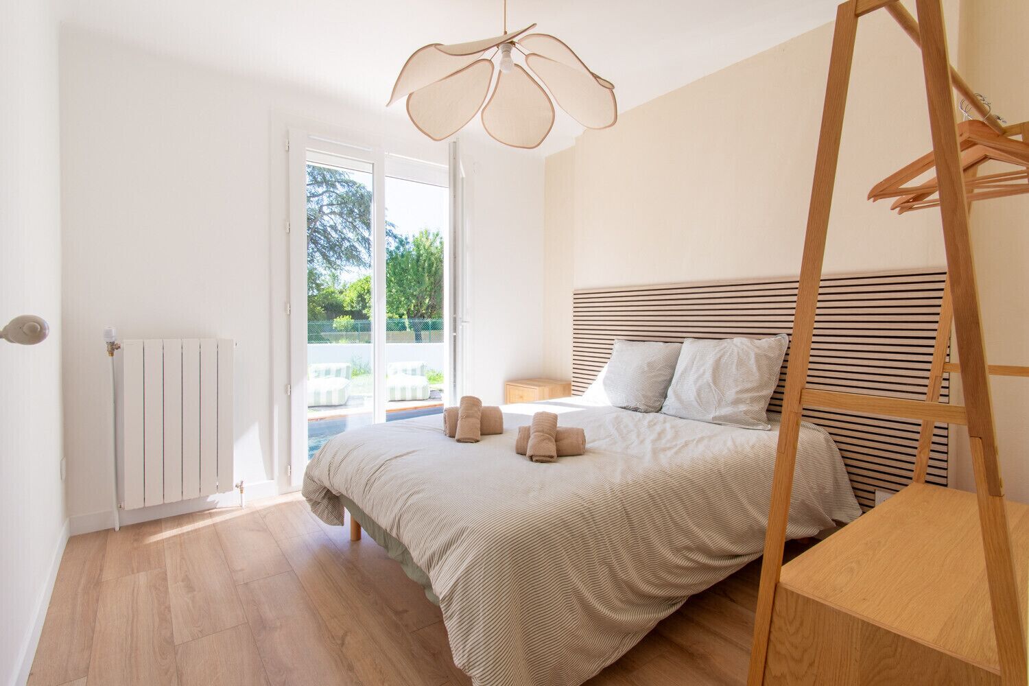 Ein Schlafzimmer mit einem Bett, einem Heizkörper, einer Holzleiter und Blick durch eine Glastür.