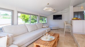 A modern living room with a sofa, wooden coffee table, and a kitchen area with a refrigerator and a TV.