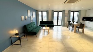 Een moderne woonkamer met een groene bank, een kleine ronde tafel, en een eethoek met een houten tafel en stoelen.