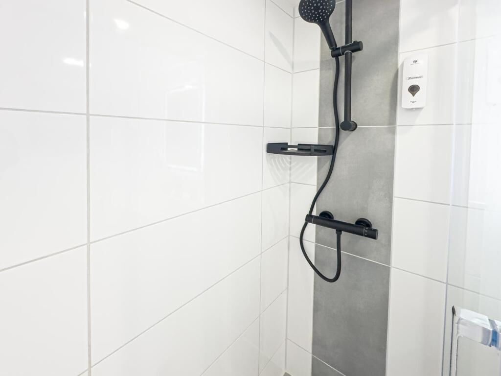 Een douche met een handdouche, een losse douchekop en een bedieningspaneel aan de muur.