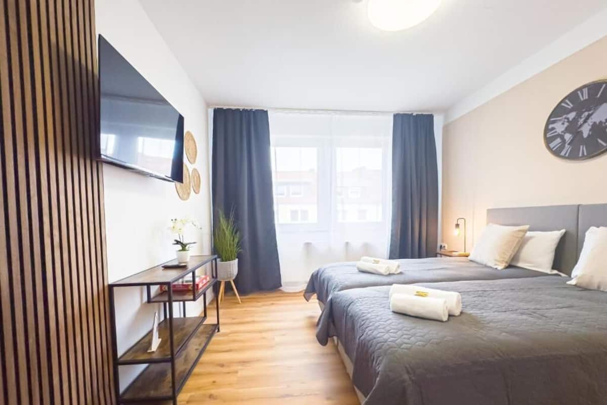 Hotellihuone, jossa on kaksi sänkyä, taulutelevisio, kello ja ikkuna, jossa on verhot.