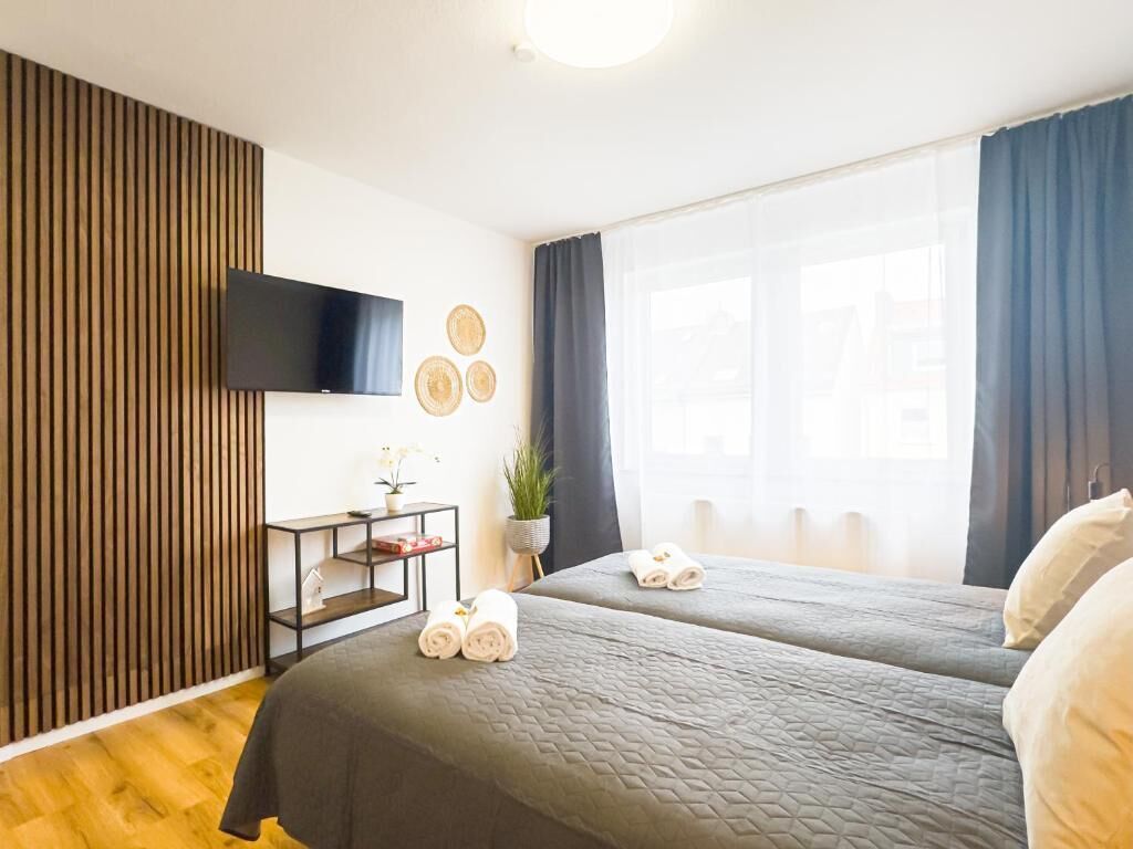 A hotel room with two beds, a TV, a desk with a plant, and a window with curtains.