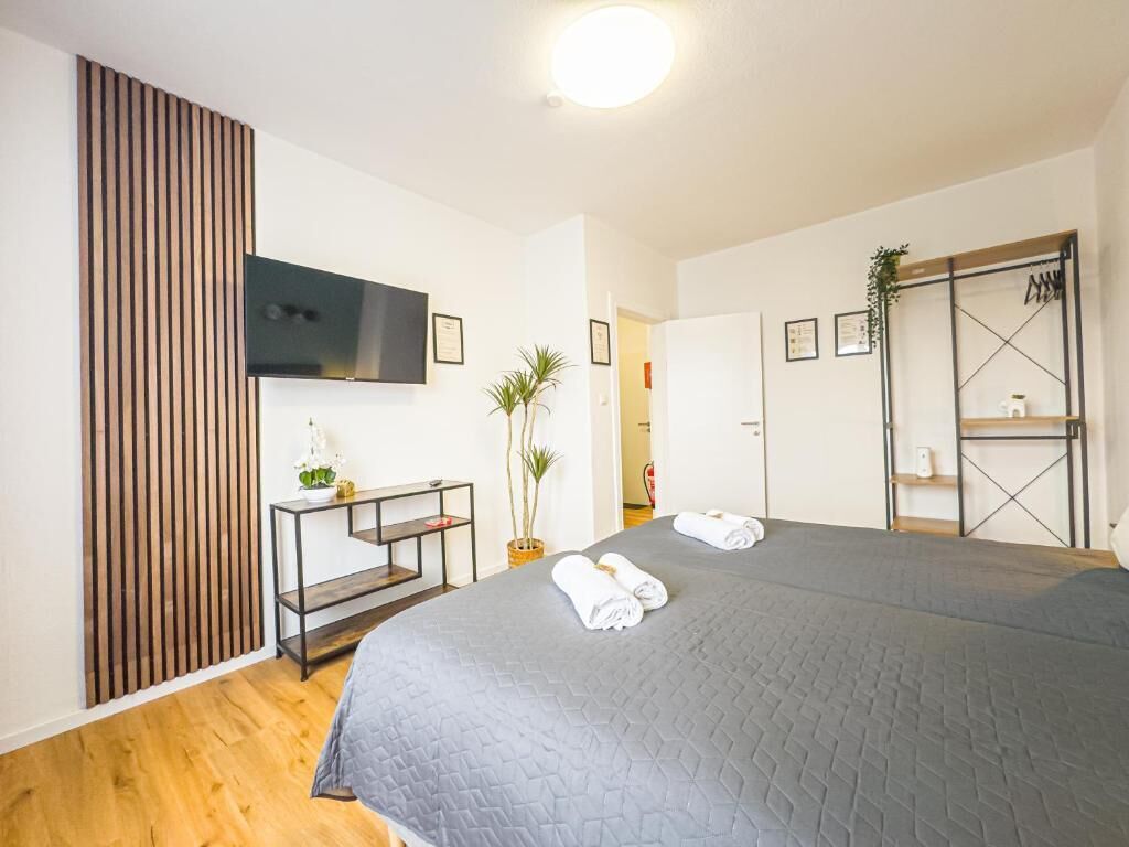 Hotelkamer met een groot bed, een aan de muur bevestigde televisie, een bureau met stoel en een plant.