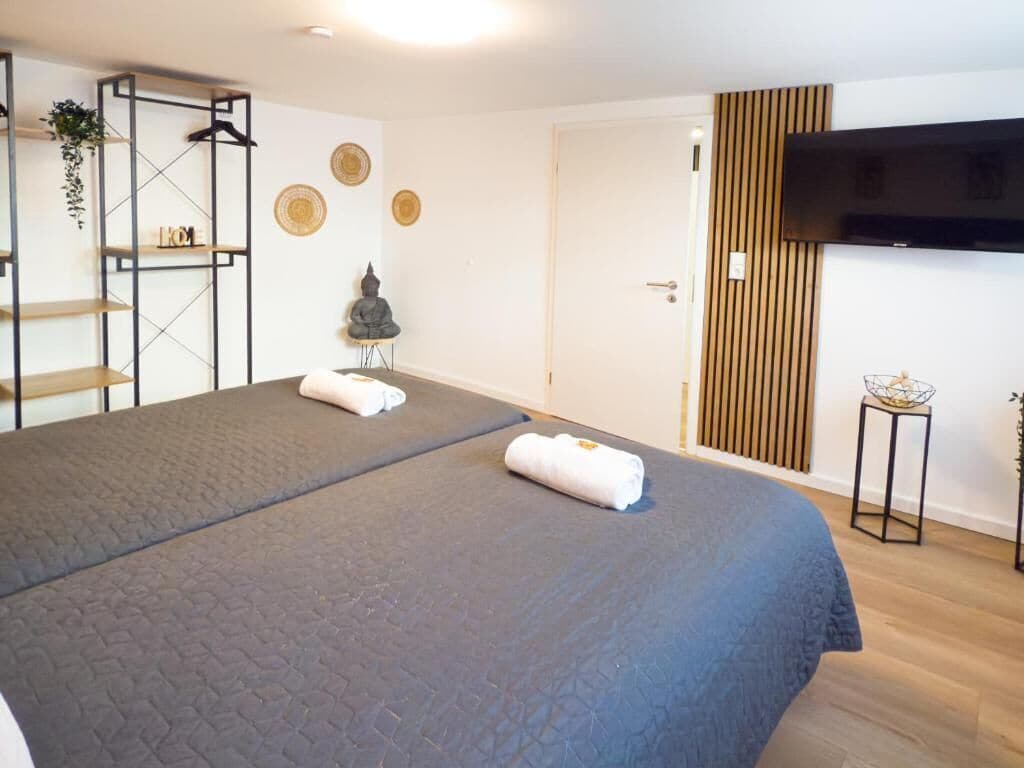A modern hotel room with a large bed, a TV mounted on the wall, and a wooden panel design.