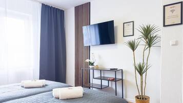 A hotel room with a bed, a TV, a small table, and a potted plant.