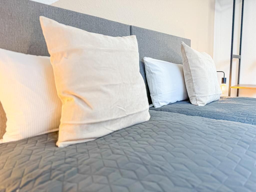A bed with a grey quilt and white pillows.