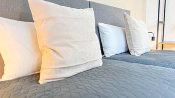 A bed with a grey quilt and white pillows.