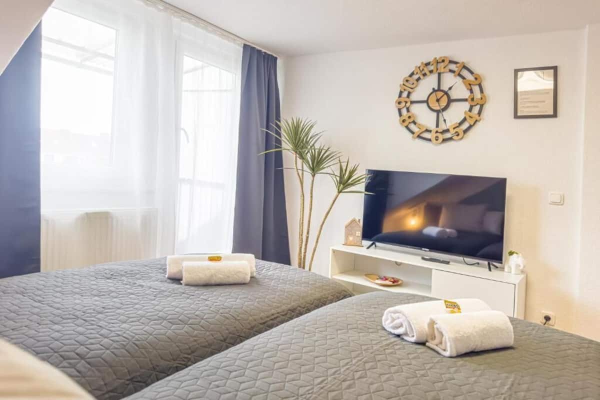 Hotellihuone, jossa on kaksi sänkyä, televisio, kello ja ikkuna, jossa on verhot.