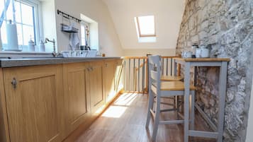 Una cocina con armarios de madera, pared de piedra, una ventana y una mesa con sillas.