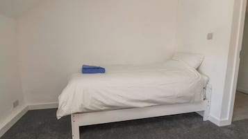 Una habitación pequeña con una cama individual, una sábana blanca y un objeto azul encima.