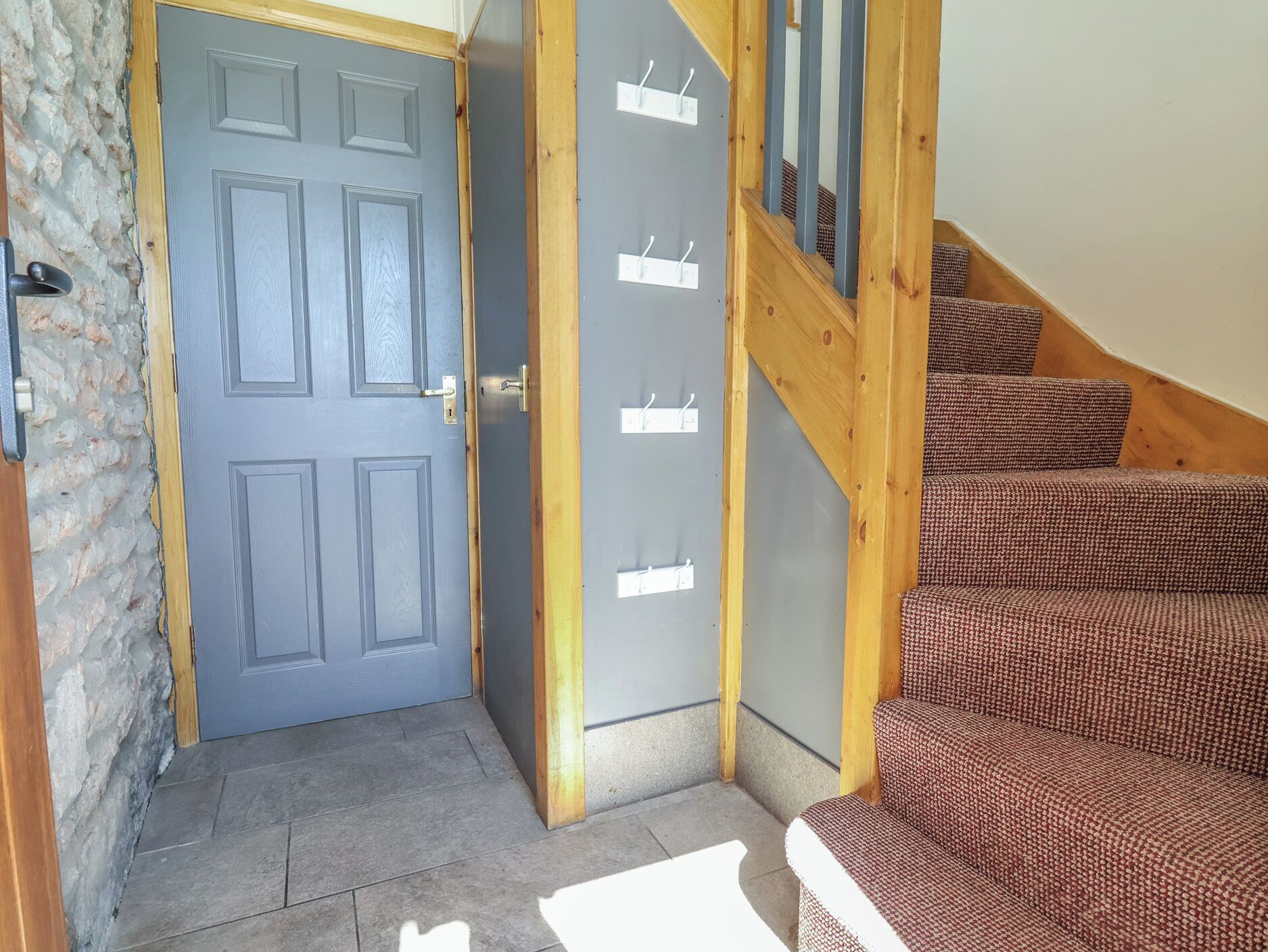 A room with a grey door, a wooden staircase, and a wall-mounted coat rack.